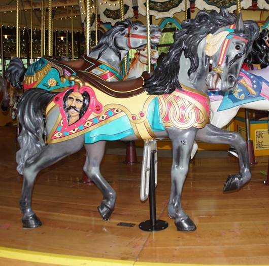 A group of people standing in front of a carousel horse

Description automatically generated
